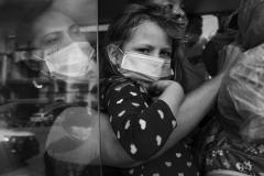 A child watches out from a bus window in Honduras, close to the border with Guatemala, on January 15, 2021.
Despite COVID-19-related border closures, refugees and migrants from Central America continued to flee their countries and head north throughout 2020 and 2021. 
In November, 2020 after hurricanes Eta and Iota hit Central America, flooding and mudslides left 9,3 million victims, of which 3,5 million are children (UNICEF), fueling a significant migration to the United States.
As a ten thousand people caravan gathered in San Pedro Sula in the night between January 14 and 15, the photographer has documented their northward journey, following several families through Guatemala, Mexico, and the United States for seven months in 2021.
The scene depicted in the photograph happened in a gas station parking lot, where the cars and buses were stopping to pick people up. The people on the bus welcomed photographers and journalists to work.