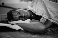 A man lies down in a charity shelter in Tenosique, Mexico, on March 8, 2021.
The shelter, active since 2011, was named The 72, in memory of 72 people from Central and South America killed by a Mexican cartel while trying to cross into the United States from the bordering Tamaulipas state on August 24, 2010.
The Tamaulipas massacre occurred 150km from the Northern border. The kidnappers shot people in the back and piled them up exposed to the weather when they refused to work for the cartel.
Mexican authorities revealed that two people survived. Among them, an Ecuatorian shot in the jaw faked his death not to be shot again. 
By 2021, nine bodies remain not identified, and the crime with impunity.
The photographer visited the shelters several times in 2021, and worked with the assistance of The 72’s professionals to avoid photographs of people whose visibility would have put lives at risk.
In 2021, the number of refugees and migrants needing a safe place at night aroused beyond the shelter capacity. The chapel, adorned with 72 crosses on the main wall, was converted into a dormitory.